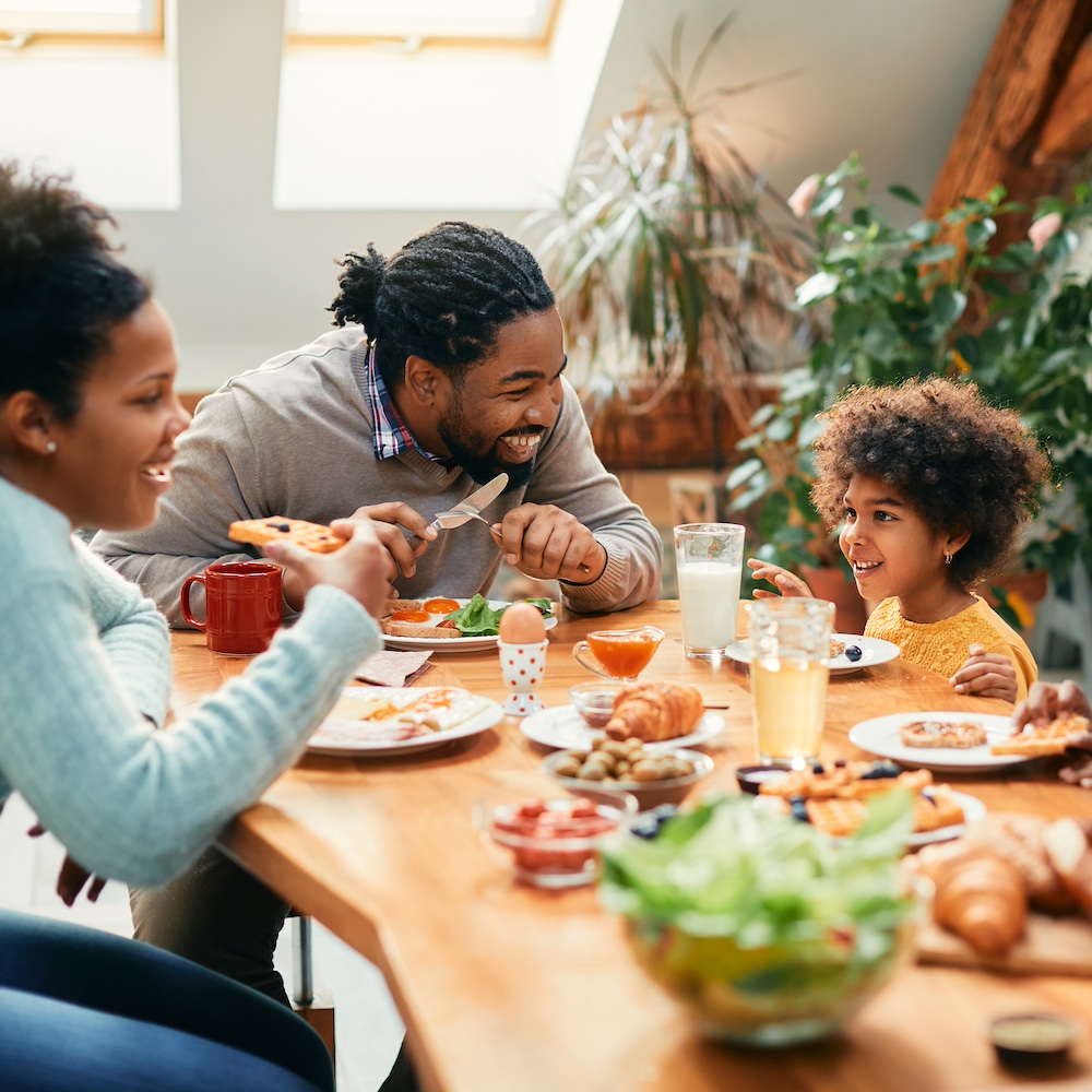 Happy African American family enjoying in conversation while eating breakfast together at dining table.