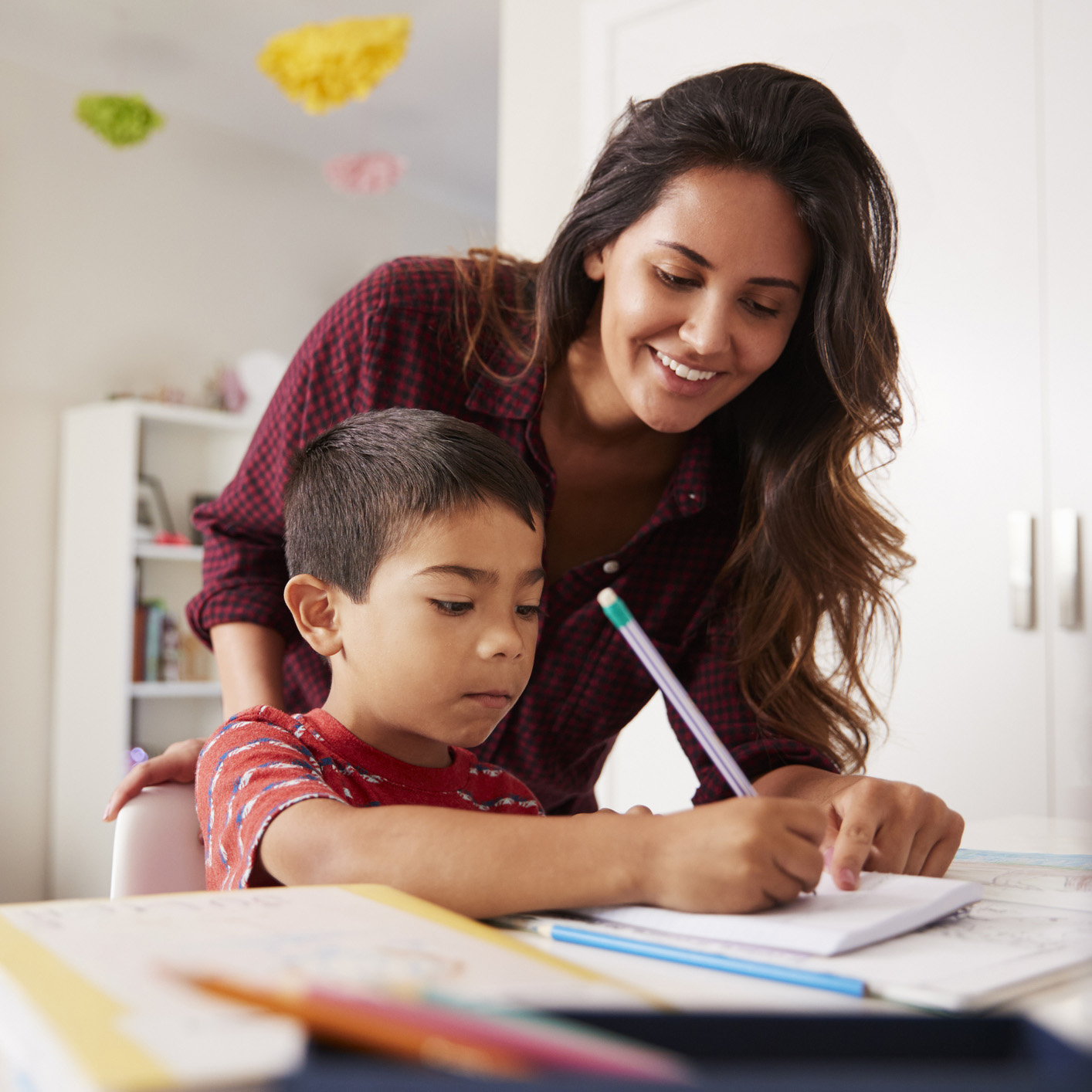 Mother Helping Son With Homework Sitting At Desk In Bedroom