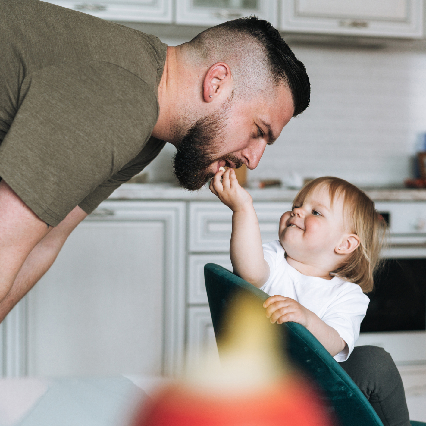 Happy father young man feeding and having fun with baby girl little daughter in kitchen at home