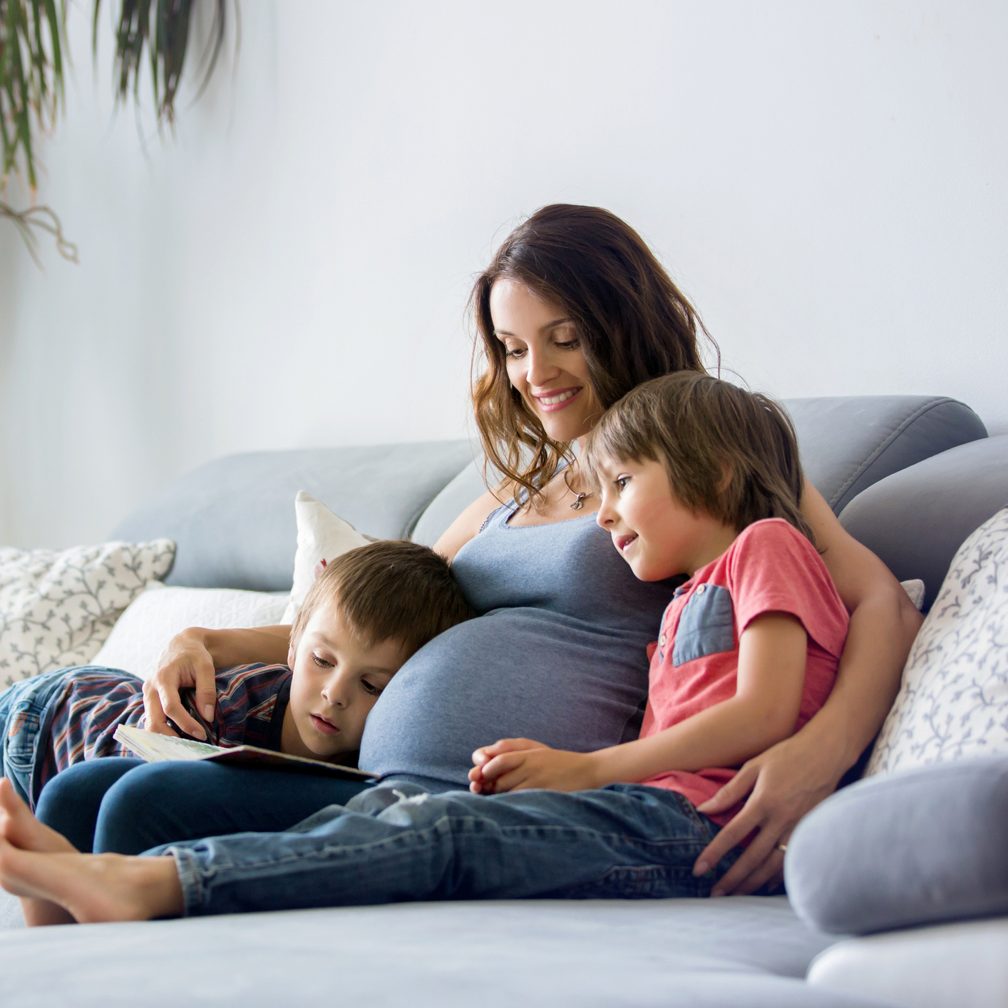 Young pregnant woman, reading book at home to her boys