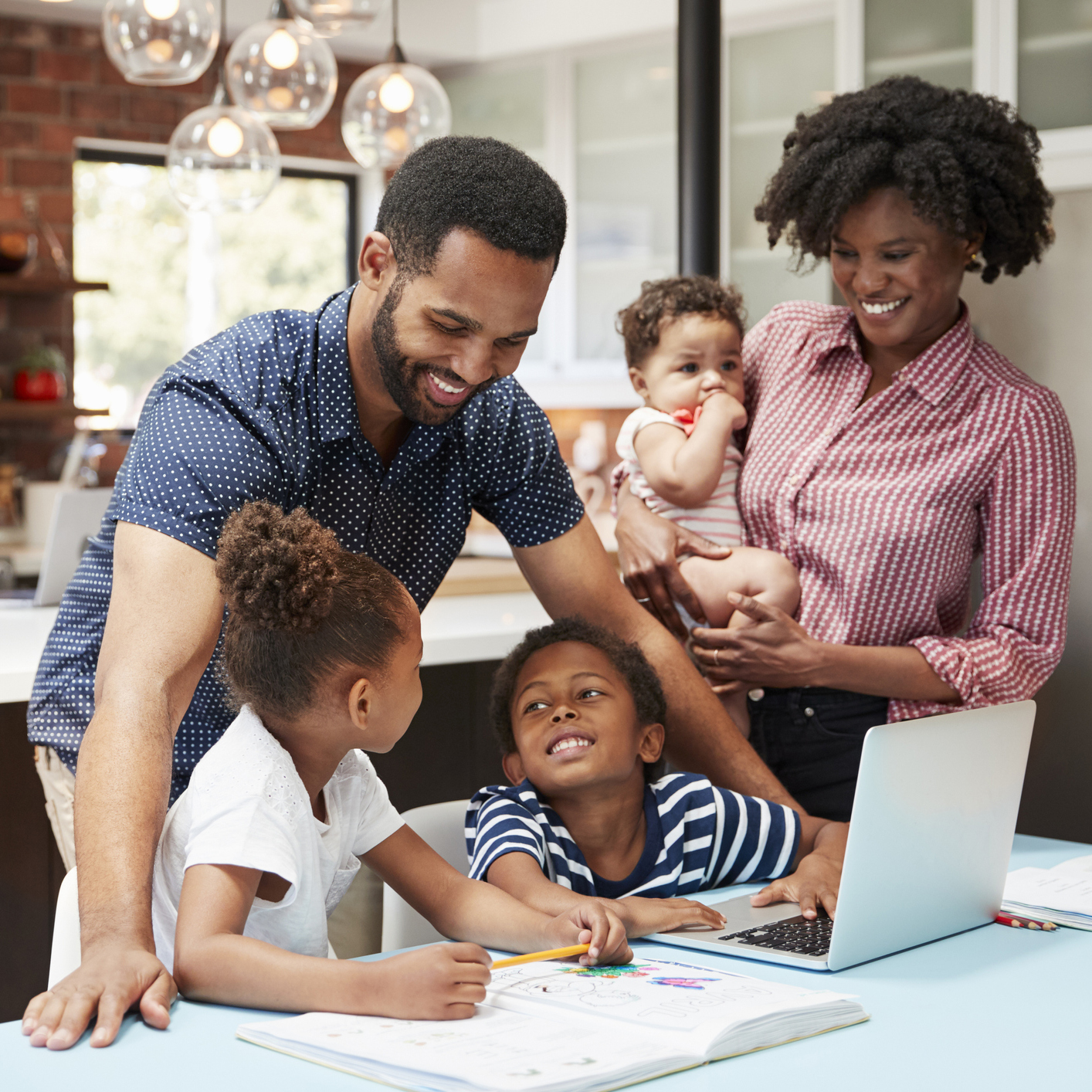 Father Helps Children With Homework Whilst Mother Holds Baby