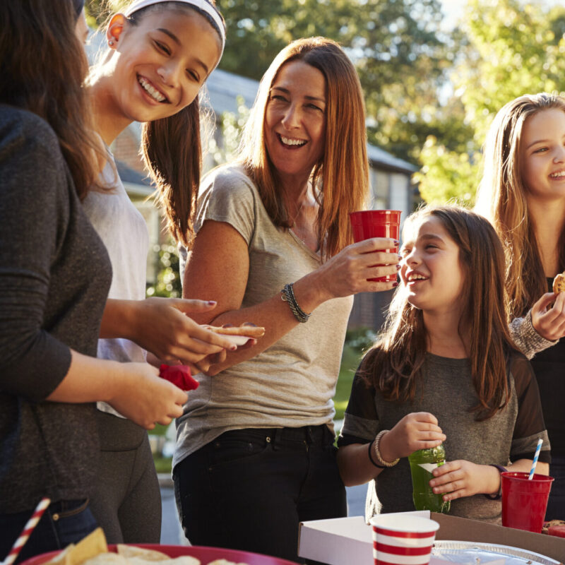 Girls stand talking at a block party food table, close up