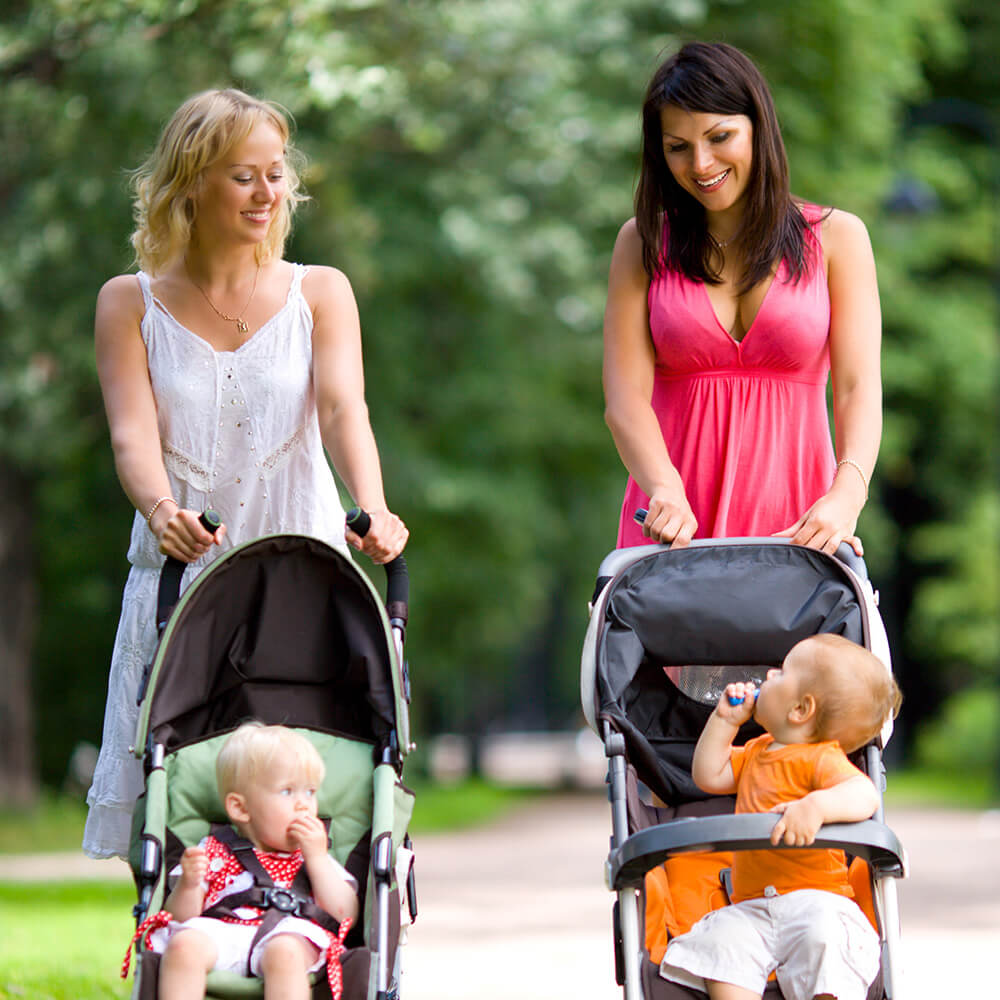 Two women walking their kids in strollers.