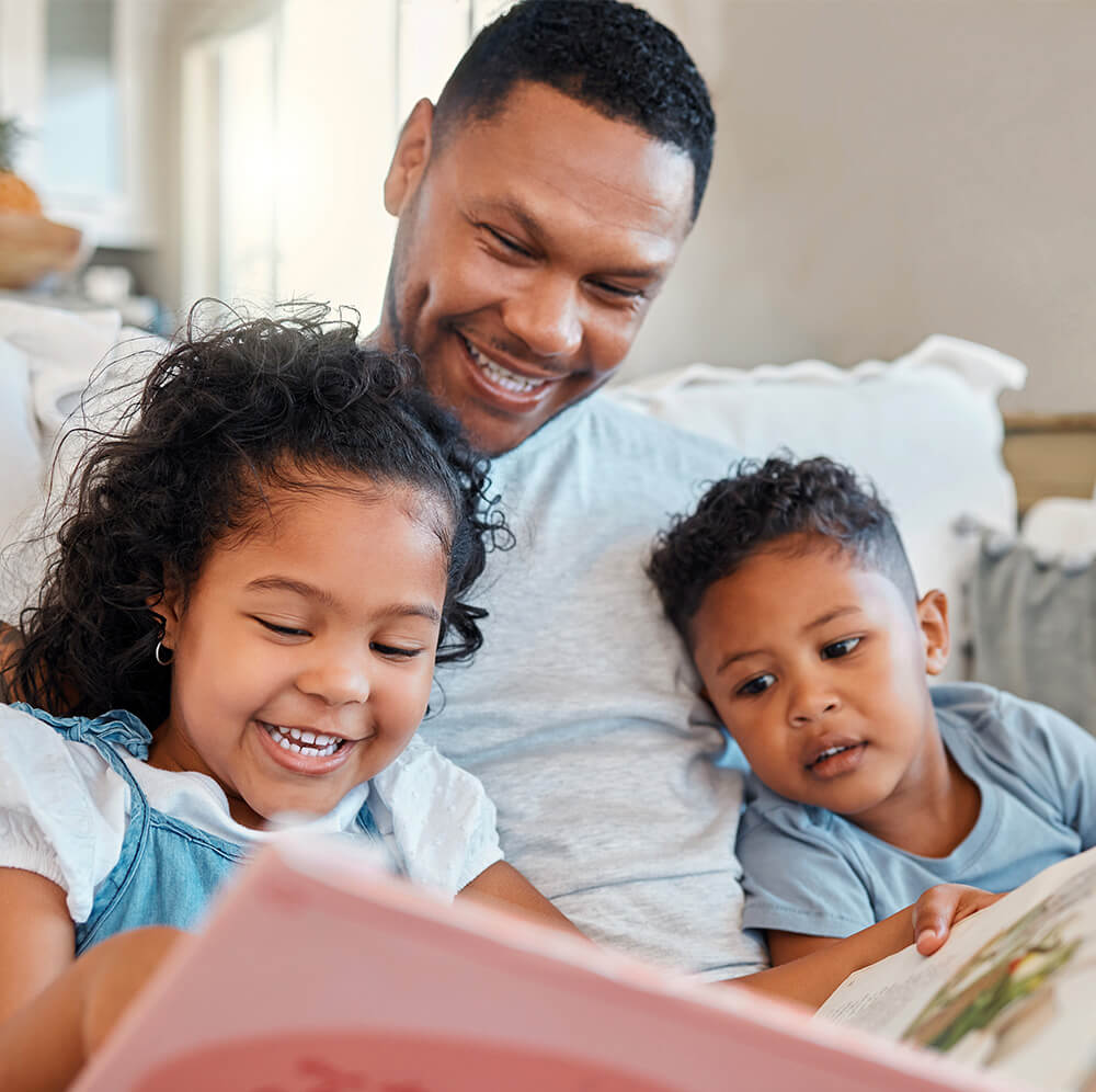 Young man reading to his kids on the sofa.