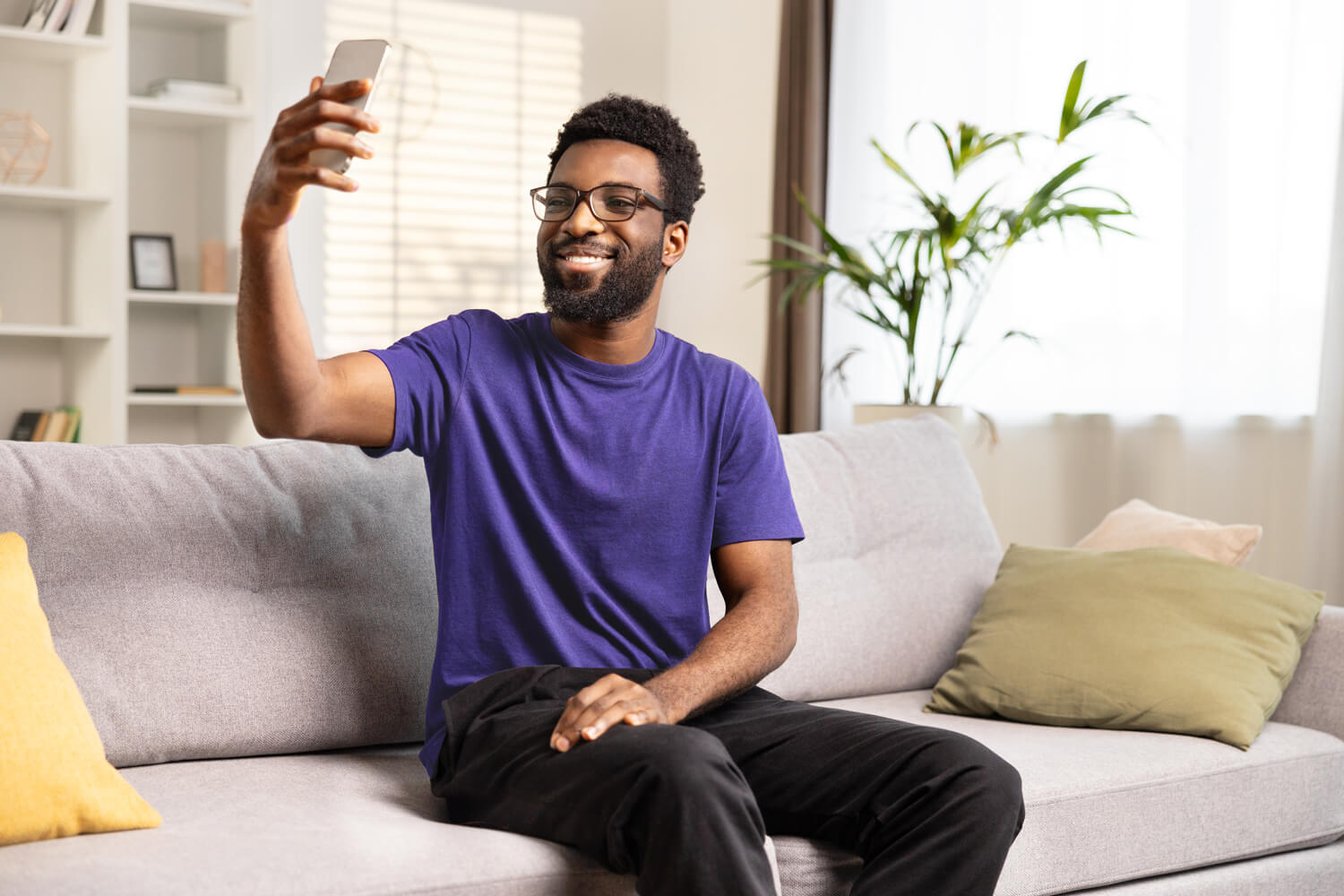 Smiling-Man-Taking-Selfie-on-Couch-violet-shirt Smiling man on a couch taking a selfie.