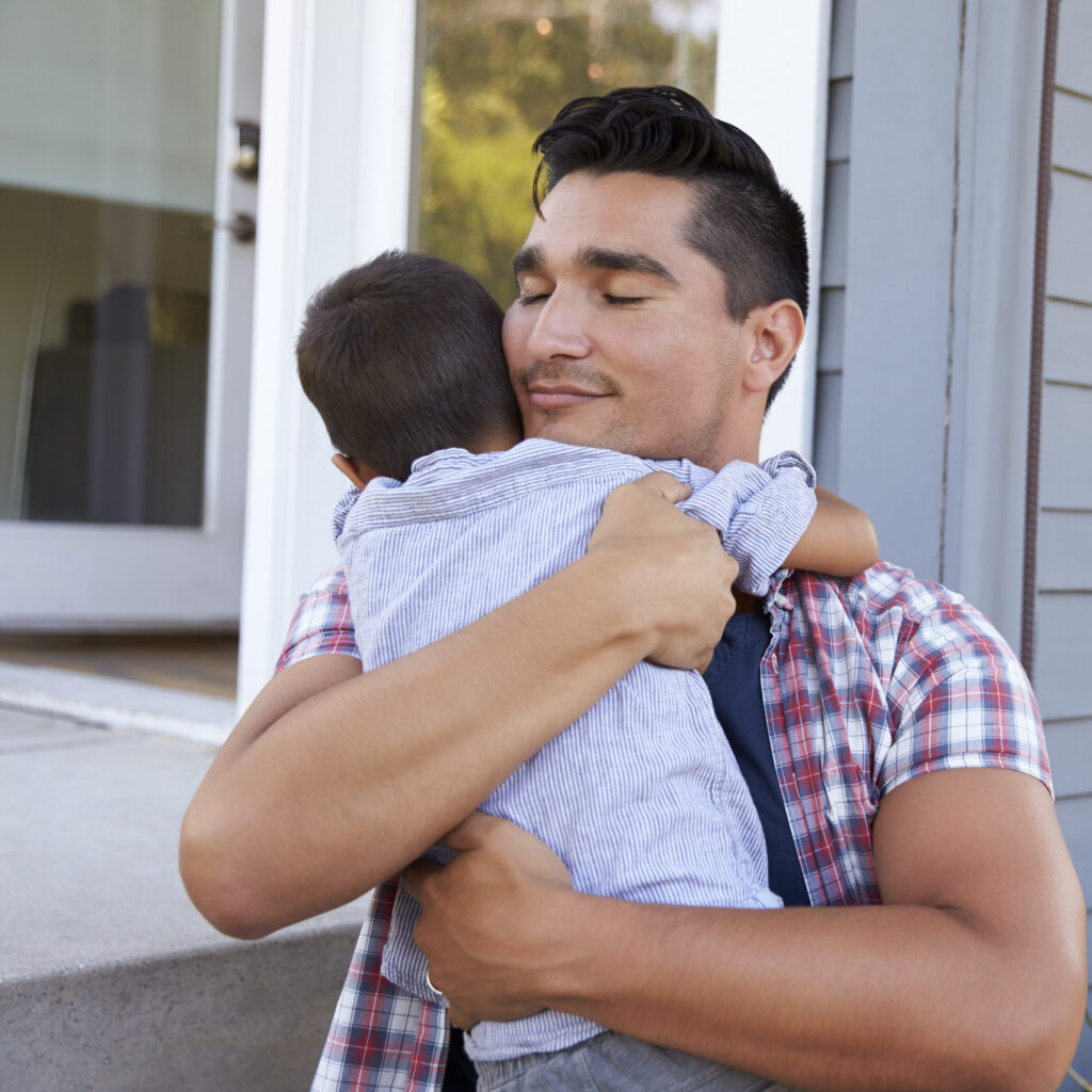 Father Hugging Son Sitting On Steps Outside Home