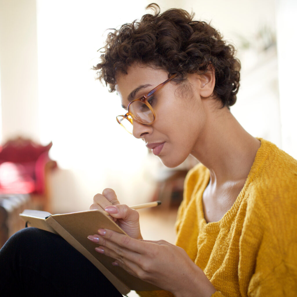 Close up young african american woman with glasses writing in book
