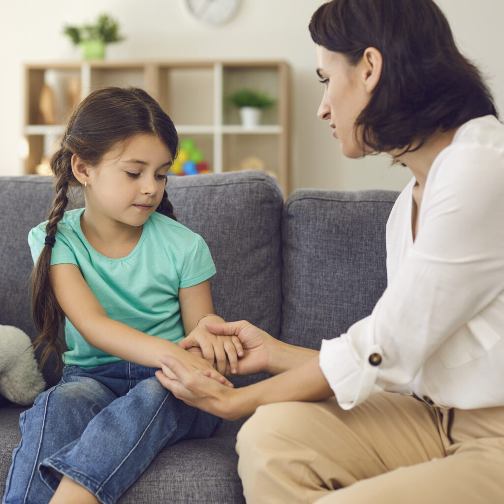 Mother sitting with daughter, holding her hands, talking to her and teaching her something