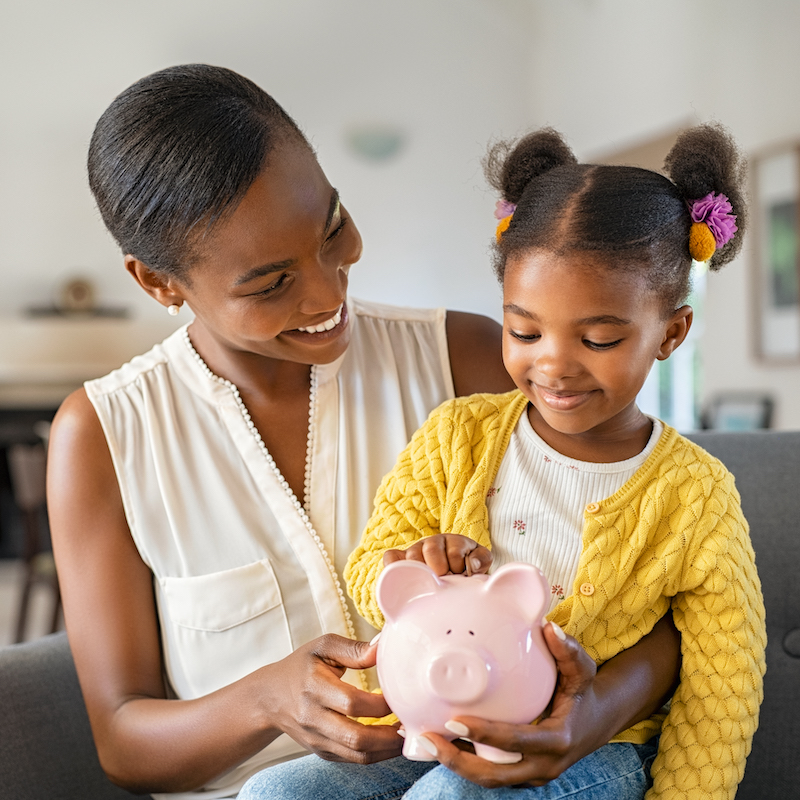 Black woman with daughter holding piggy bank