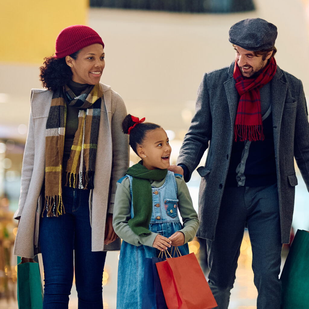 Happy black little girl and her parents buying in shopping mall during Christmas sales.