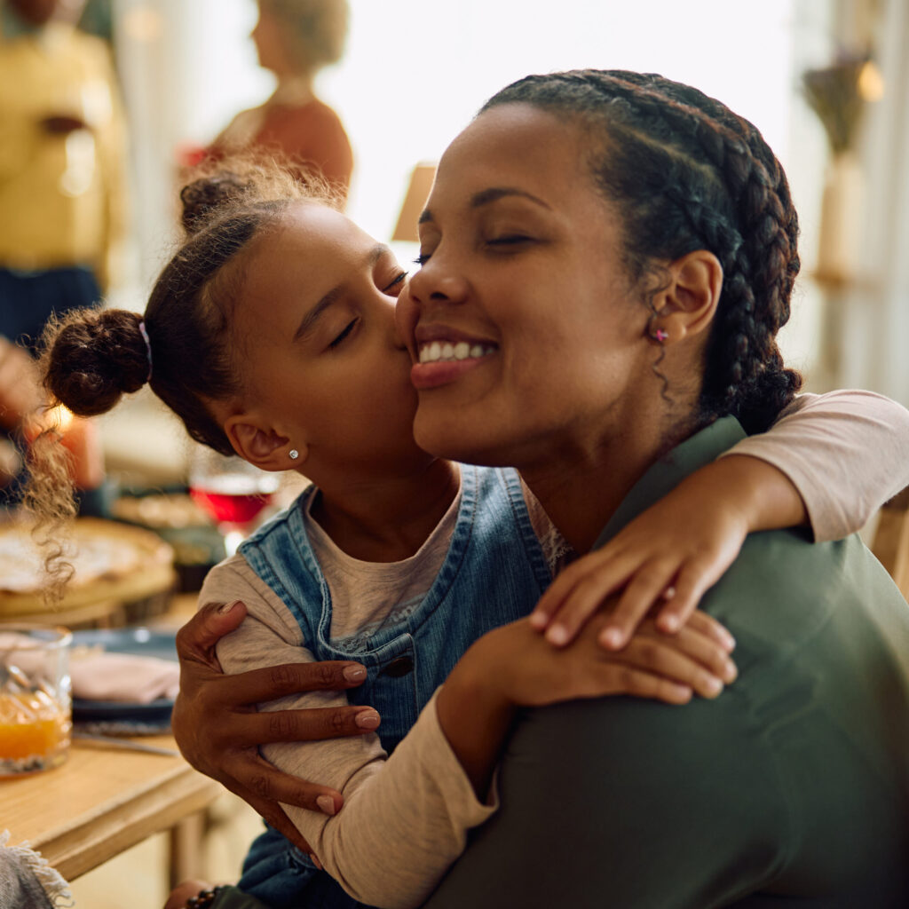 Grateful black girl kissing her mother during Thanksgiving family meal.