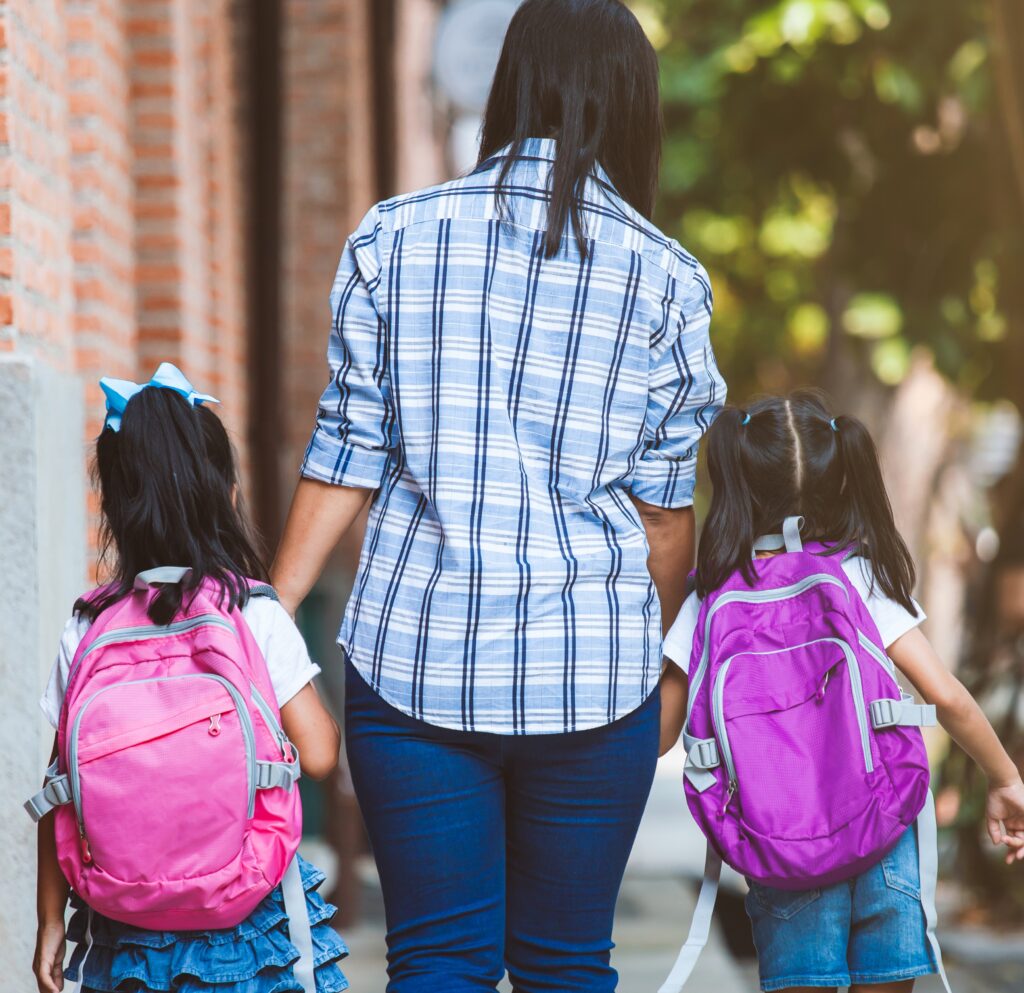Mother and daughters with backpacks holding hands and going to school togehter