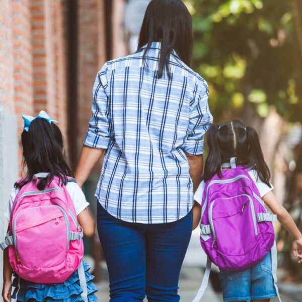 Mother and daughters with backpacks holding hands and going to school togehter